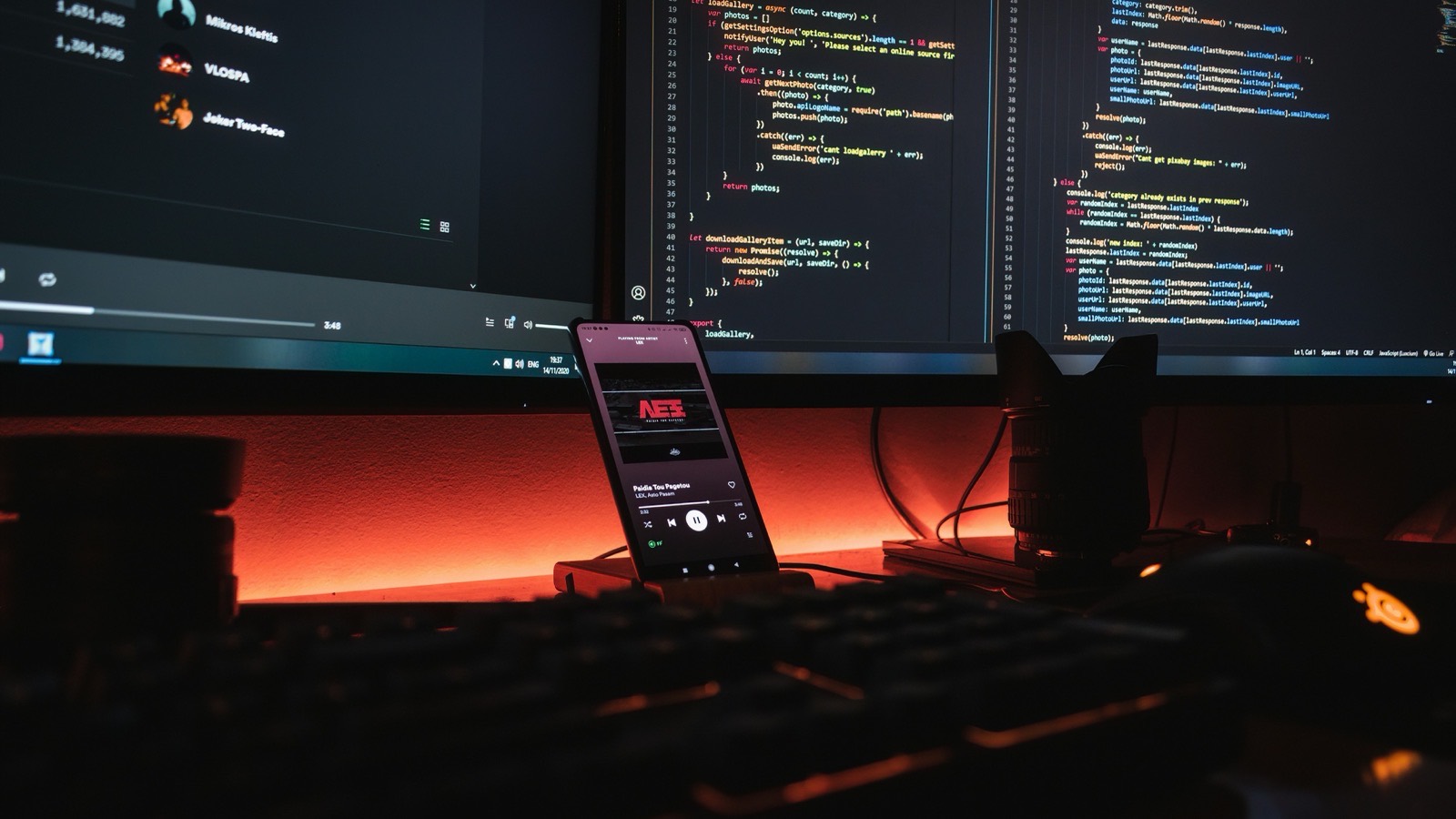 Dark desk with two monitors full of code and a phone lit by warm orange light