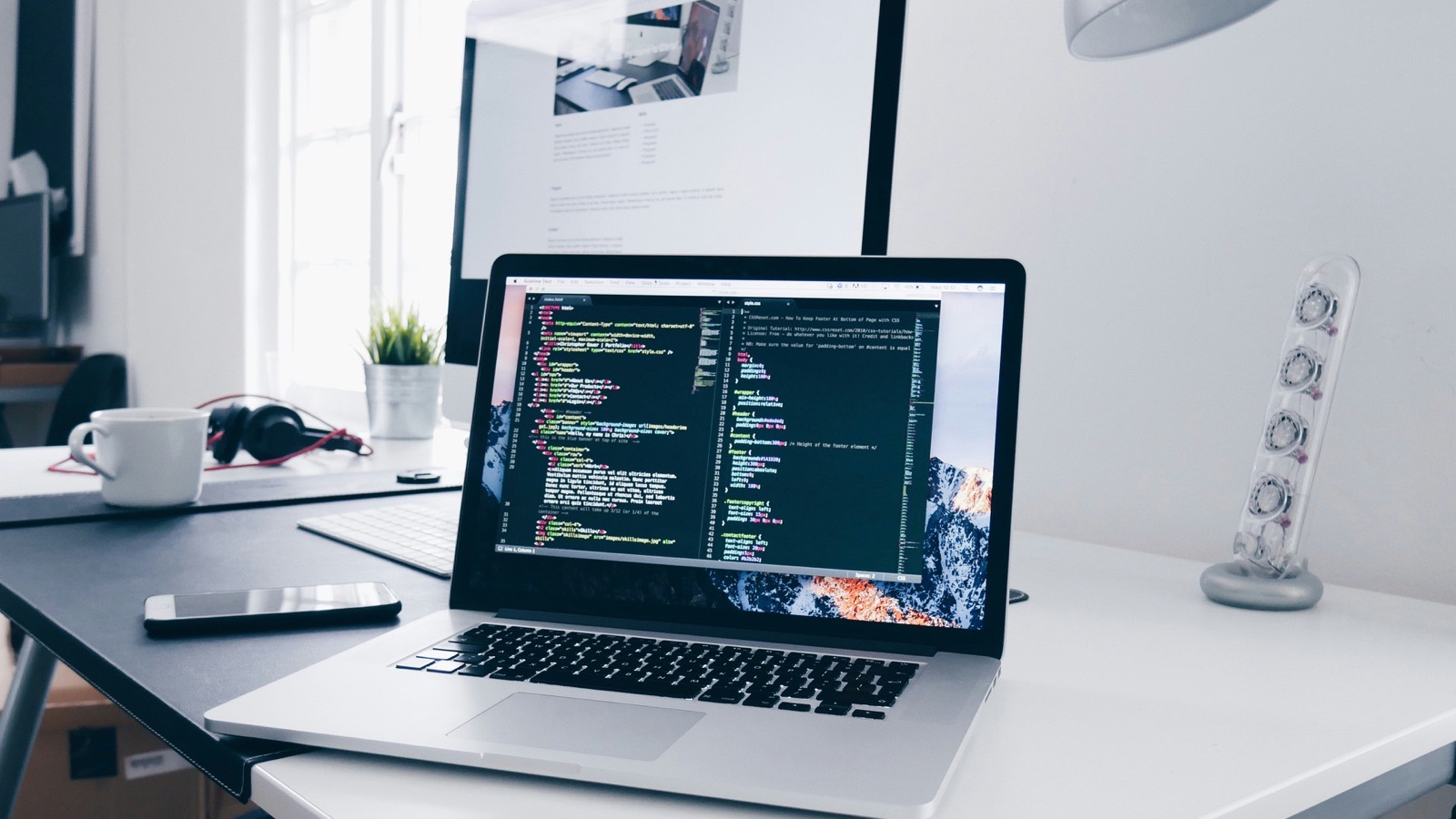 Laptop showing code on a bright, minimal desk next to a large monitor